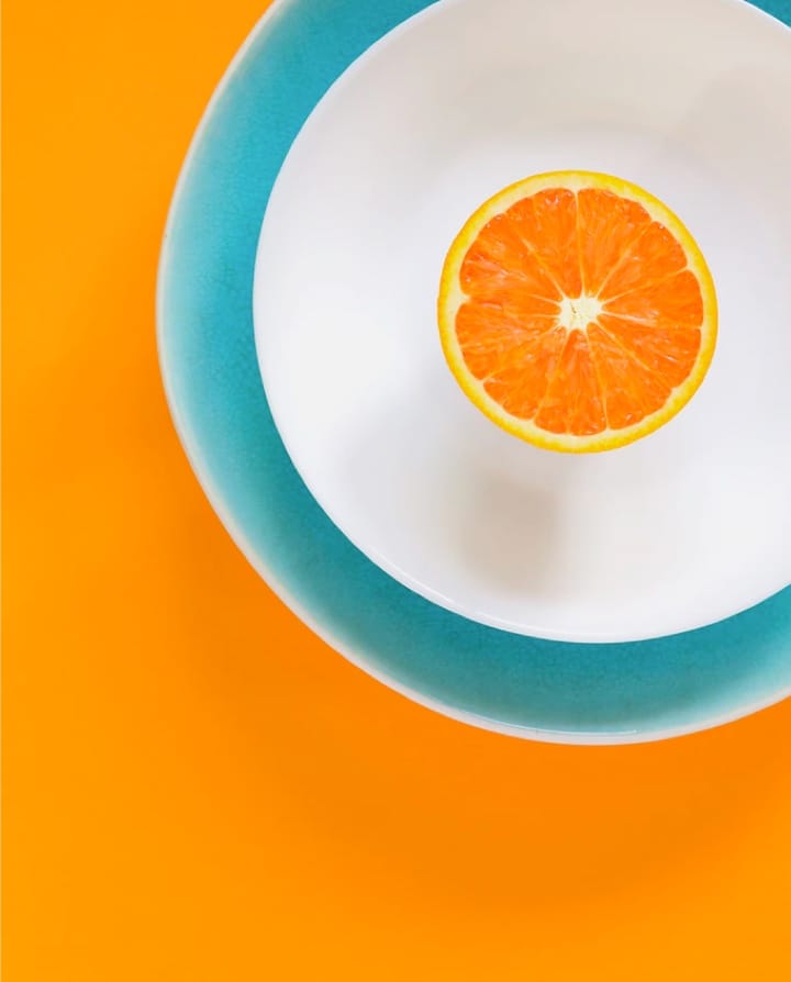 half an orange in a white dish thats inside another dish over an orange color background