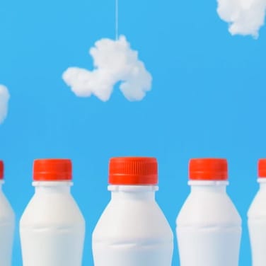 three small white milk bottles over blue background with small clouds