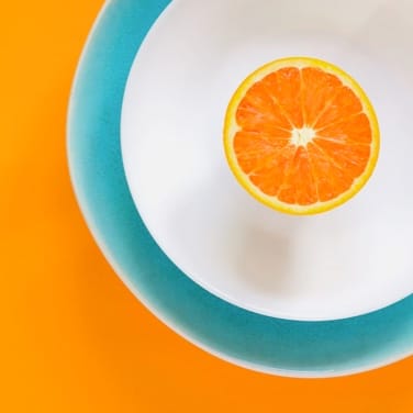 half an orange in a white dish thats inside another dish over an orange color background